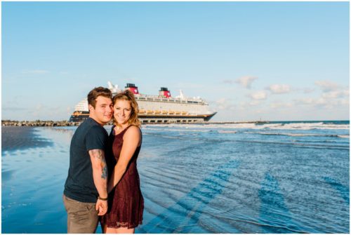 Couple smiling with Disney cruise ship in background at Jetty Park Engagement