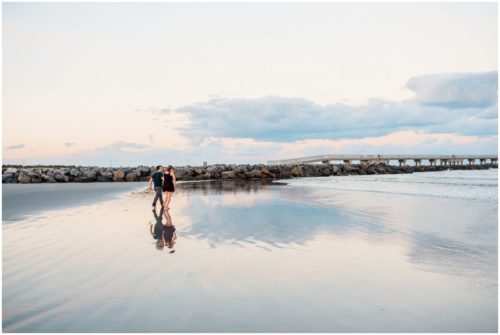 Couple walking on beach by rocks at Jetty Park Engagement