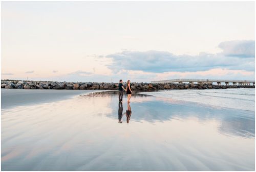 Couple walking on beach by rocks at Jetty Park Engagement