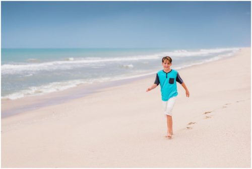 Little boy in blue walking on empty beach during their fun family beach portraits