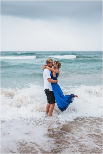 Couple hugging in water with waves crashing during storm beach engagement