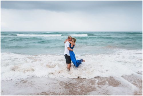 Couple hugging in water with waves crashing during storm beach engagement
