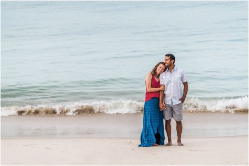 Waves rolling in as couple cuddles on beach Melbourne Beach Engagement Photography