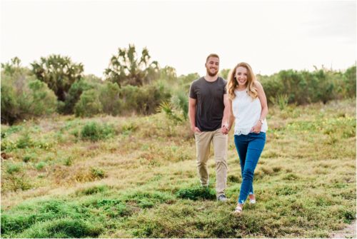 couple walking in field during Floridana Beach engagement