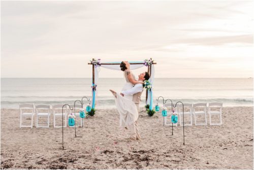 Groom lifting bride in front of arch during Cocoa Beach Sunrise Wedding
