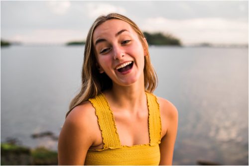 Girl in yellow top laughing at camera by the water