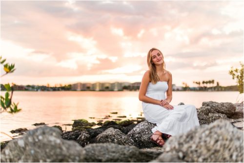 Girl in white dress sitting on rocks by river