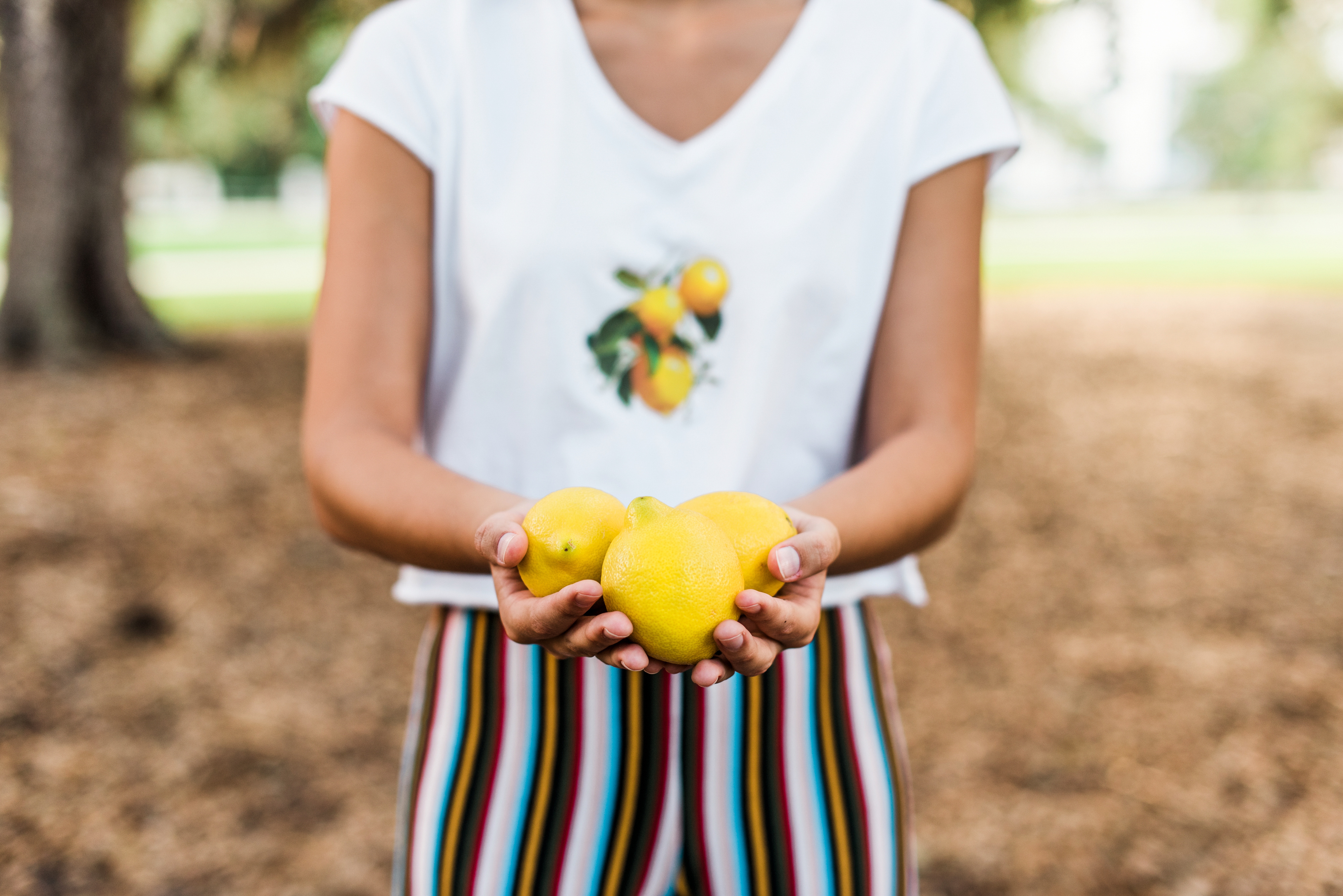 girl with lemon on shirt holding lemons in riverside park