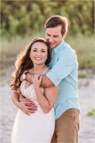 Couple hugging on Cocoa Beach with dunes in background Best Engagement Session Beach Locations