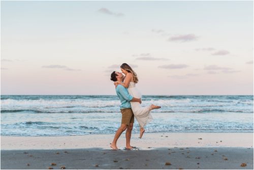 Man lifting girl up by edge of ocean