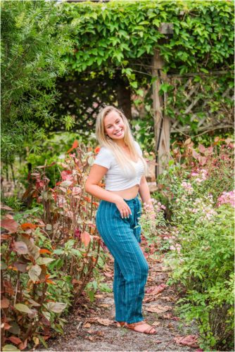 Senior in blue pants and white crop top in garden during senior portrait session