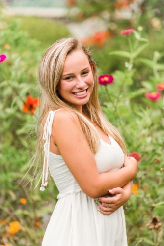Senior in white dress with pink, red and orange flowers in the background Senior Photography at Rockledge Gardens