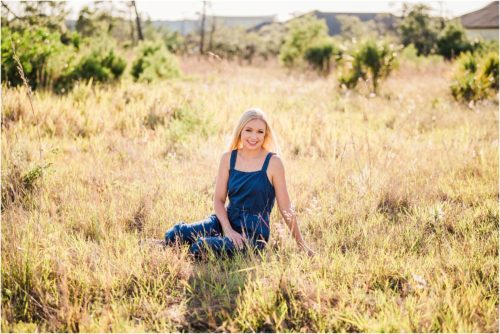 Girl in blue romper sitting in field during senior portraits