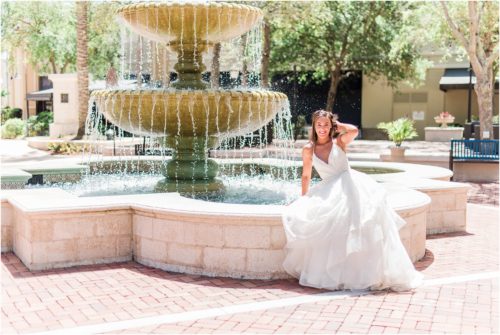 Bride sitting on edge of fountain in wedding dress by Haley Paige
