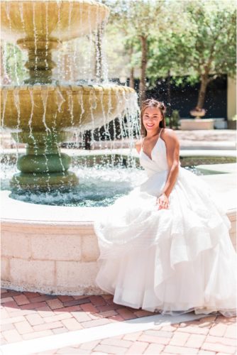 Bride sitting on edge of fountain in wedding dress by Haley Paige