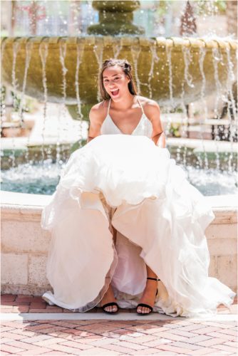 Bride sitting on edge of fountain lifting her Haley Paige wedding dress up. Melbourne Florida Wedding Photographer