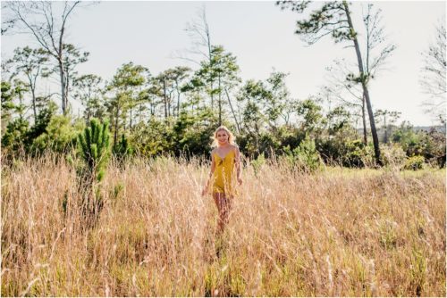 High School Senior in yellow dress waling in field with tall grass