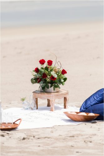 beach blanket setup with red roses and blue pillows during surprise proposal on Cocoa Beach
