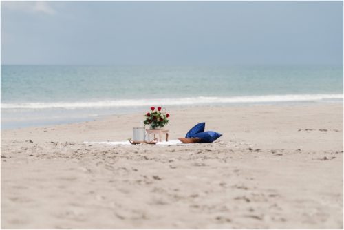beach blanket setup with red roses and blue pillows during surprise proposal on Cocoa Beach