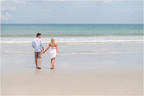 Couple walking hand in hand toward the edge of the ocean after Surprise Proposal