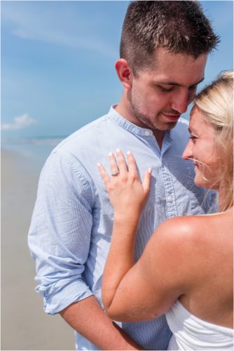 Couple hugging on beach and showing off engagement ring
