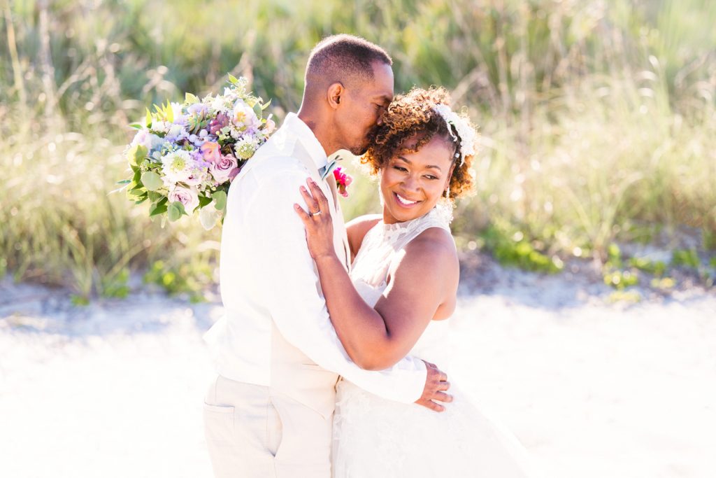 couple hugging on the beach with a purple bouquet