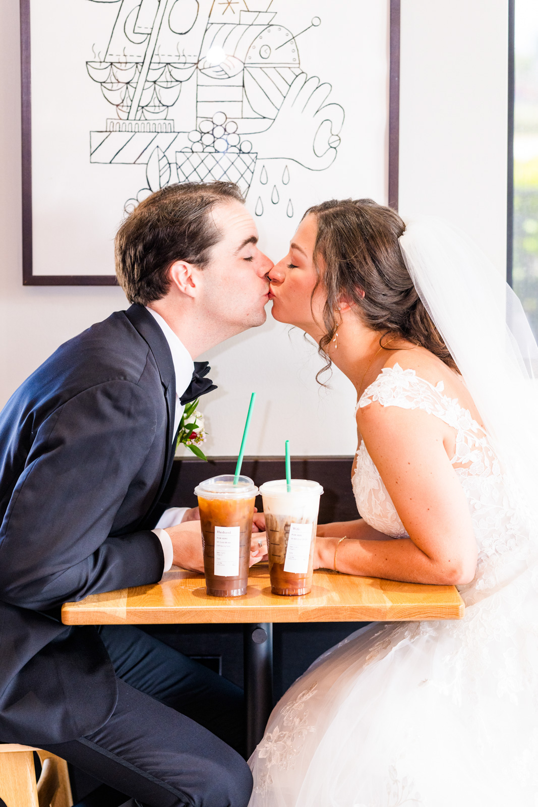 Couple in Starbucks sharing a kiss over a cup of coffee in their wedding clothes