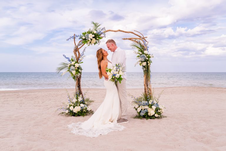 Bride and groom embracing under a floral driftwood arch on Melbourne beach