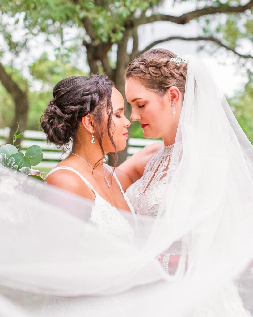 Two brides embracing beneath a wedding veil at an outdoor Florida wedding at Up the Creek Farms