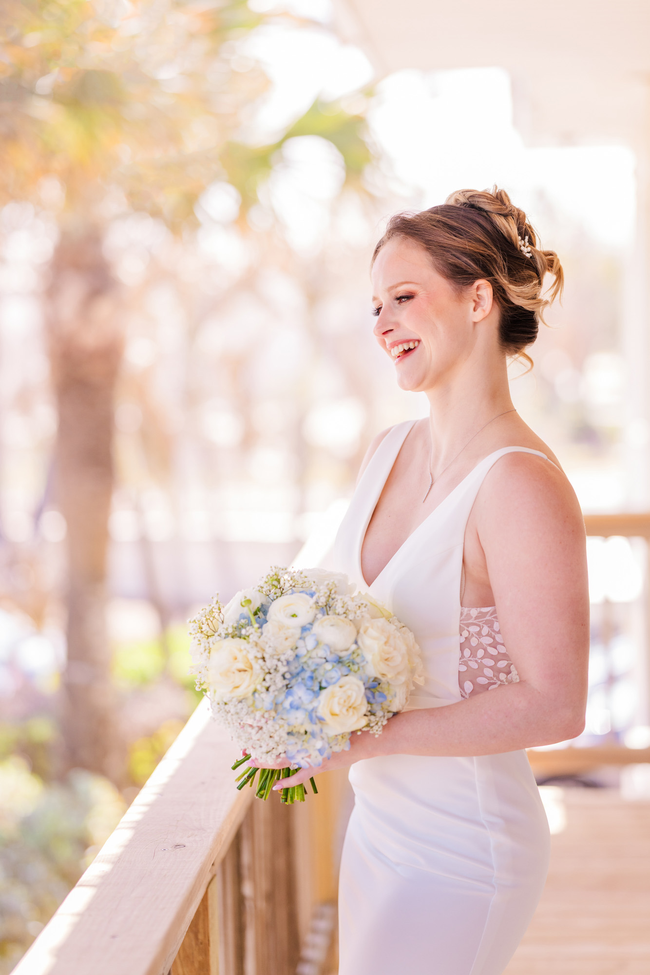 Bride laughing while holding a white and blue wedding bouquet on a sun