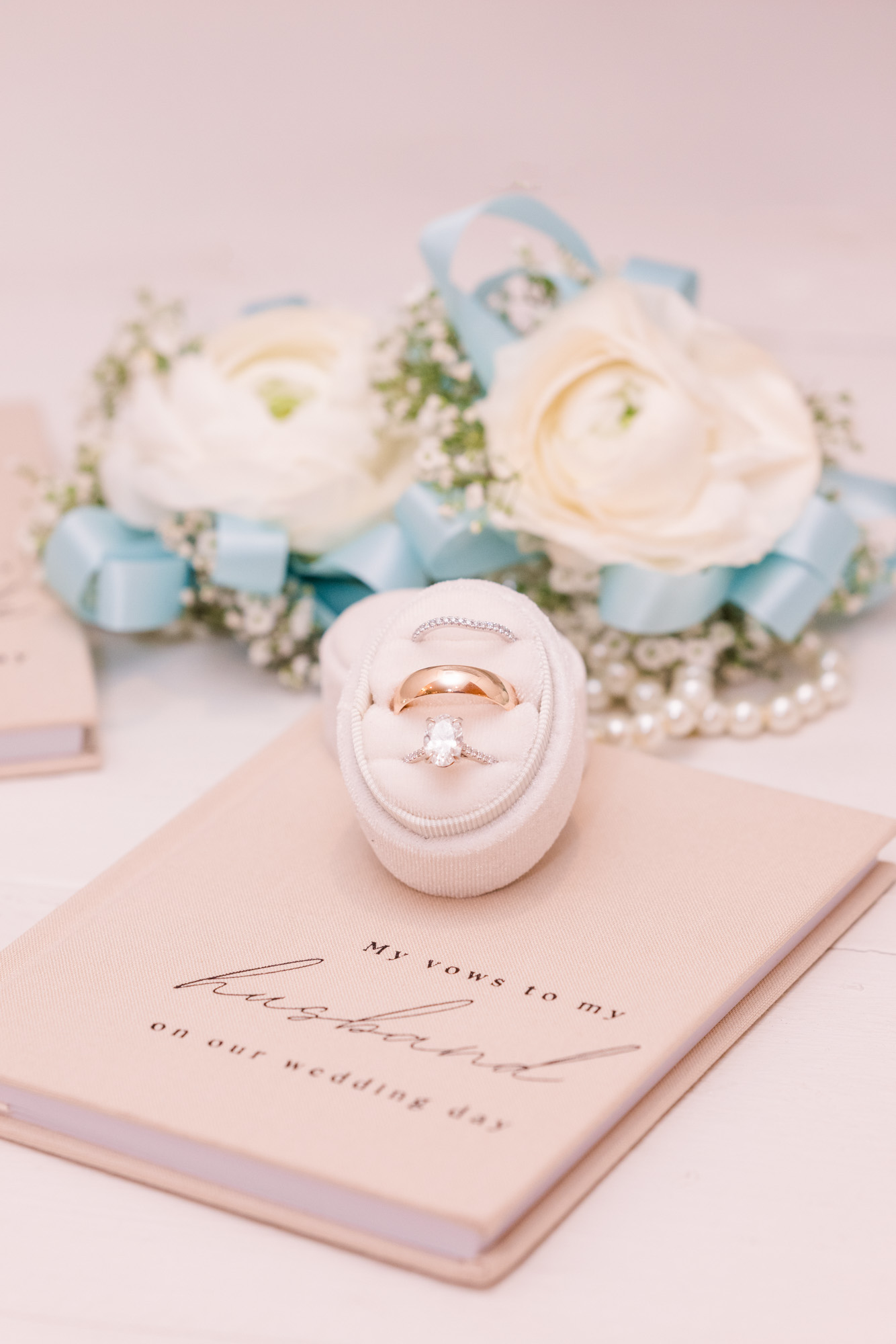 Wedding rings displayed on a vow book with white flowers and pale blue ribbon.