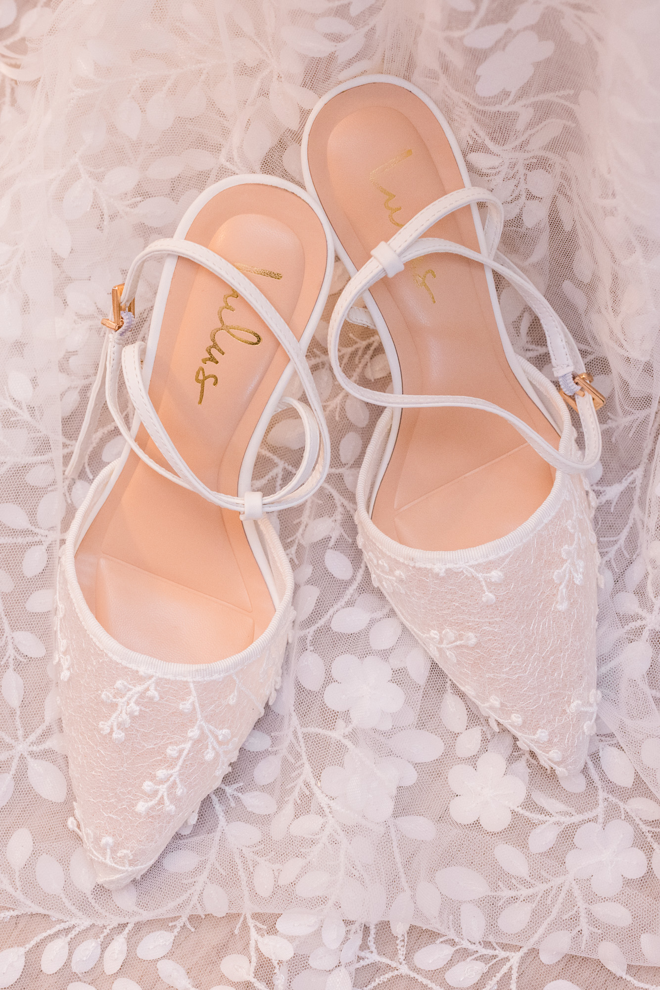 White lace wedding shoes arranged on the bride’s wedding dress.