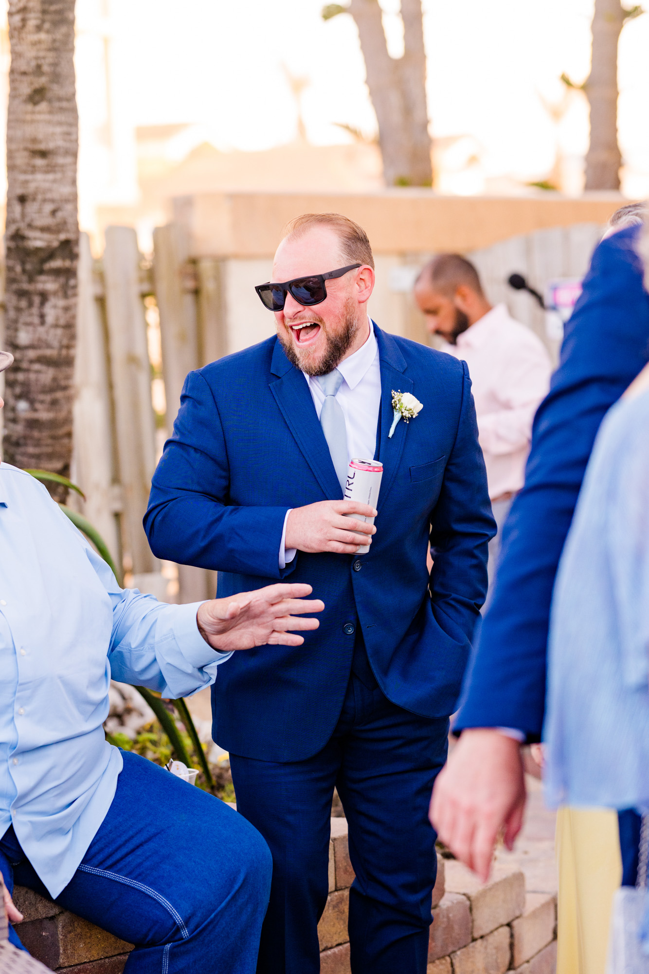 Groomsman in a navy suit laughing during cocktail hour at Harbour House Oceanfront.