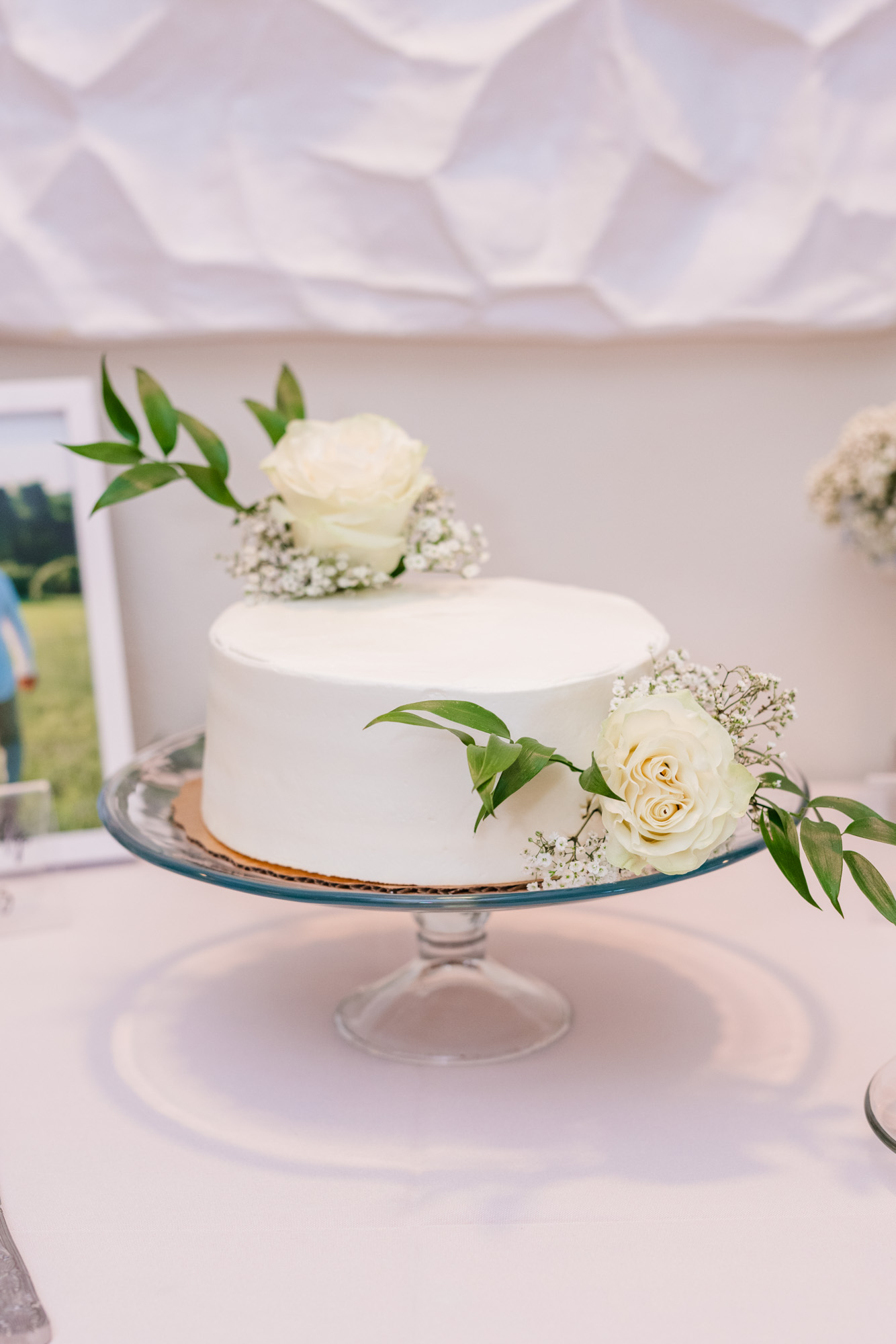 Simple white wedding cake decorated with white roses and greenery.