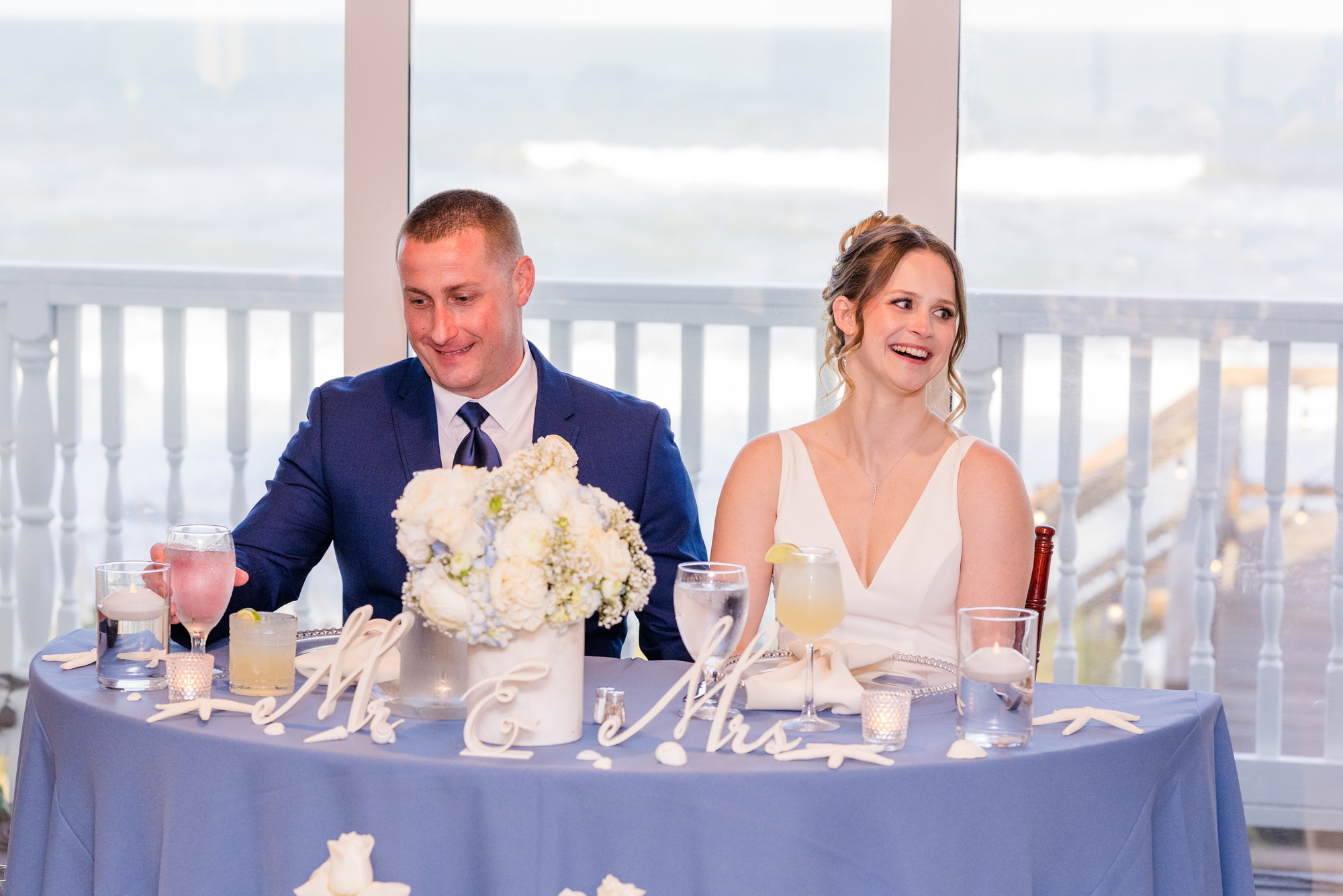 Bride and groom seated at their blue sweetheart table overlooking the ocean.