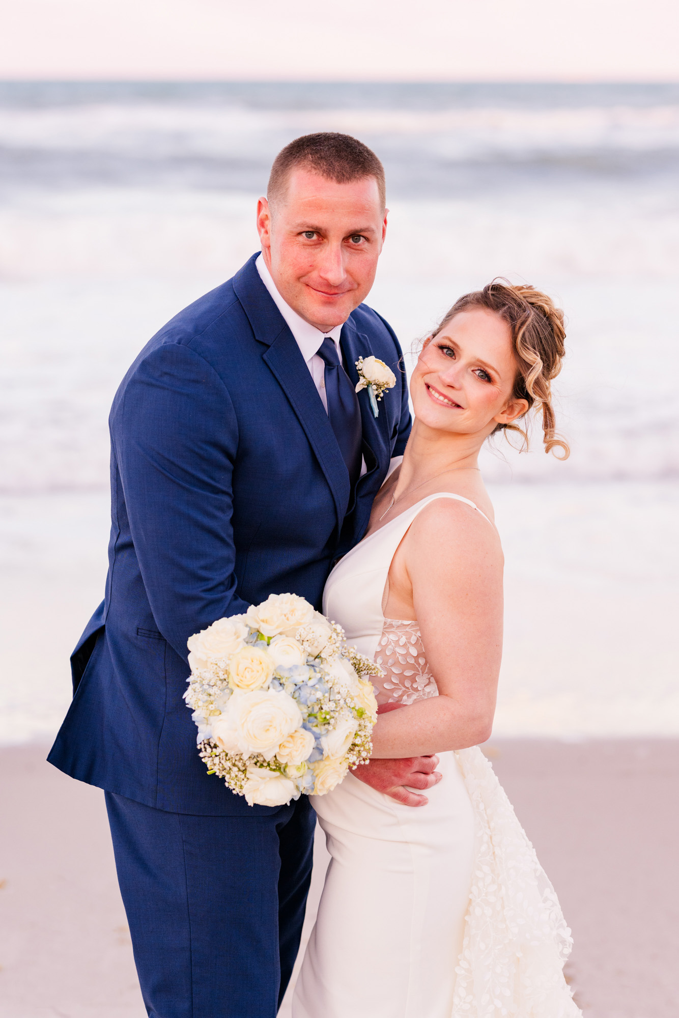 Close portrait of the bride and groom on the beach with a white and blue bouquet.