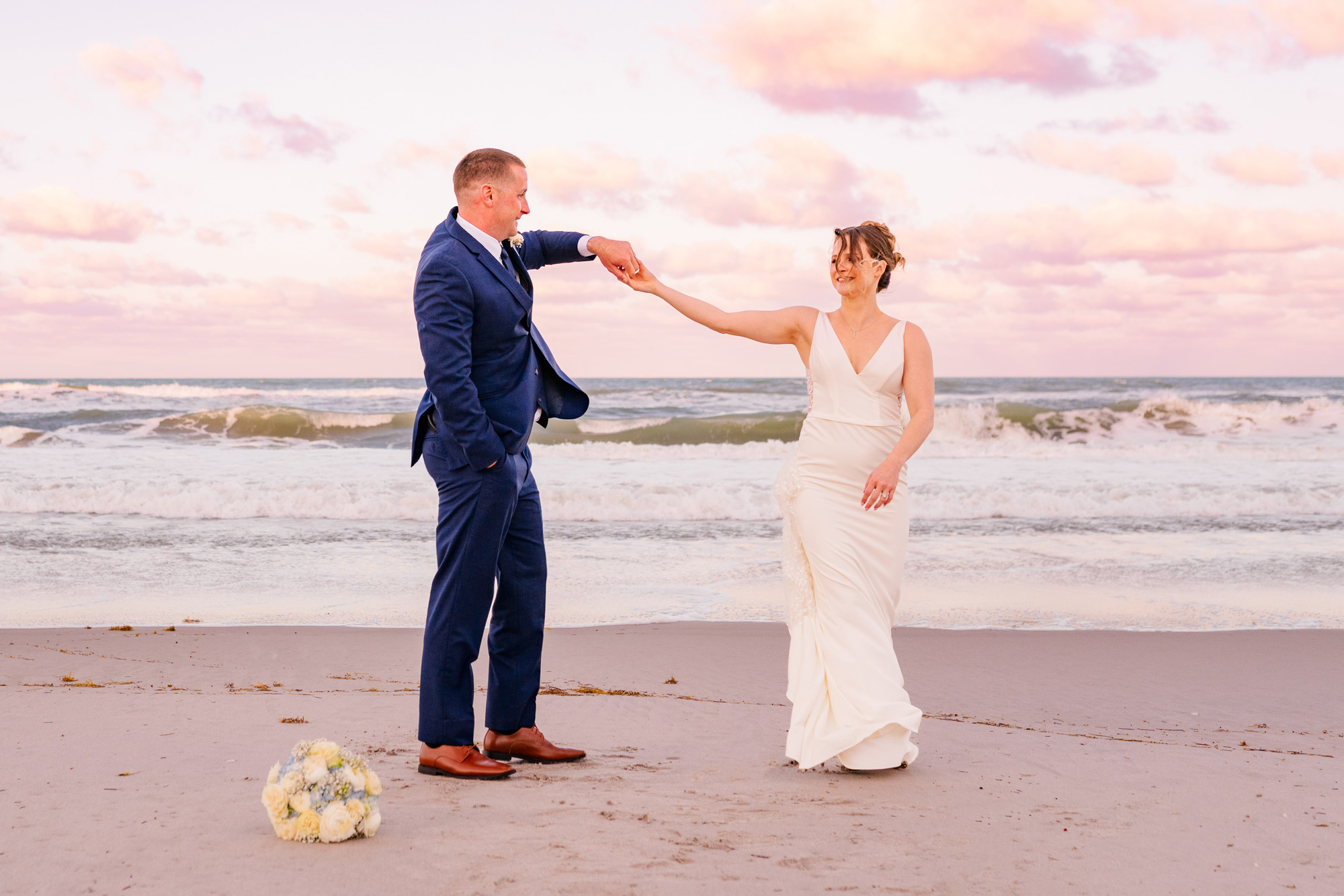 Bride and groom holding hands while walking and playing on the beach after their wedding.