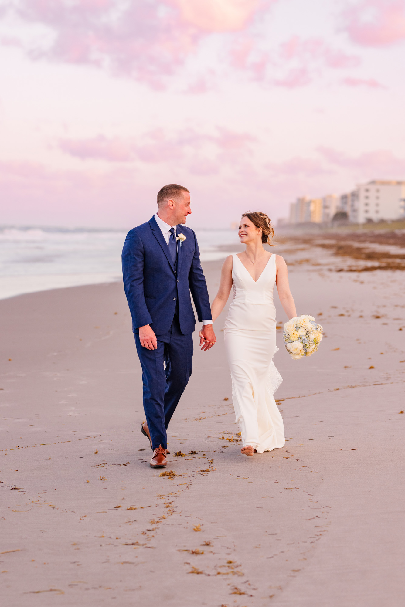 Bride and groom smiling at each other while walking on the beach after their Harbour House Oceanfront wedding.