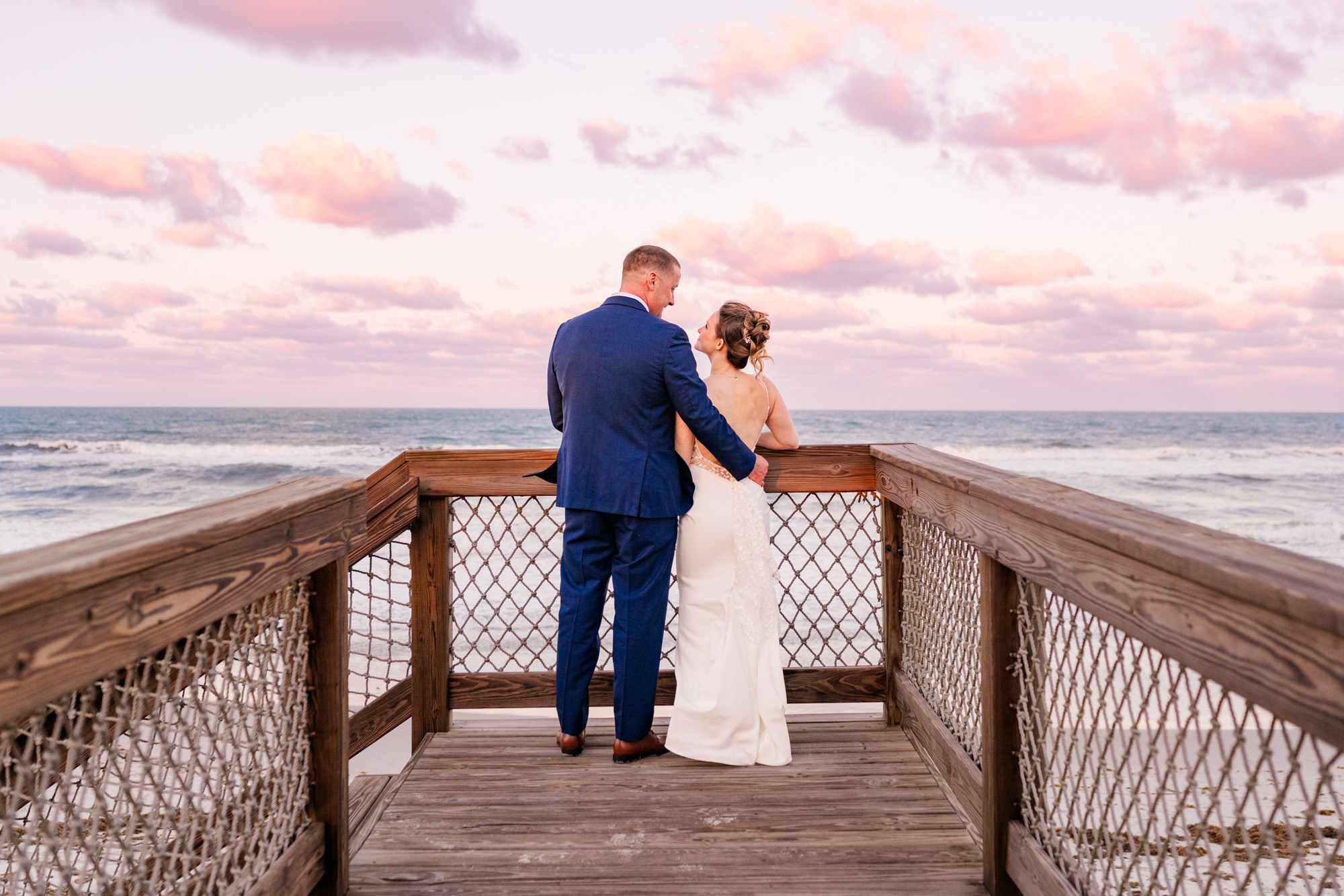 Bride and groom kissing on a wooden boardwalk overlooking the ocean.