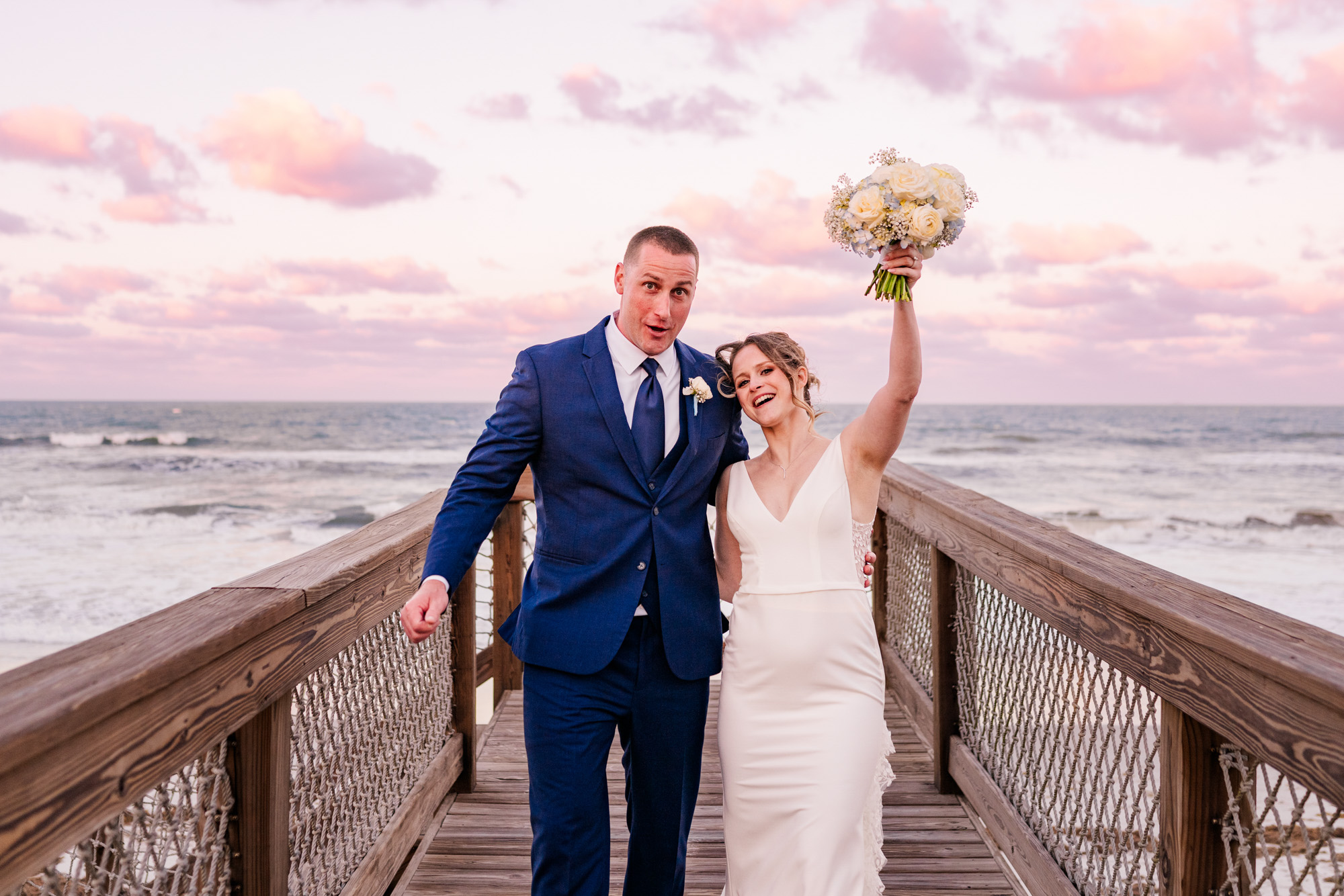 Newlyweds celebrating on the boardwalk with the bride holding her bouquet overhead.