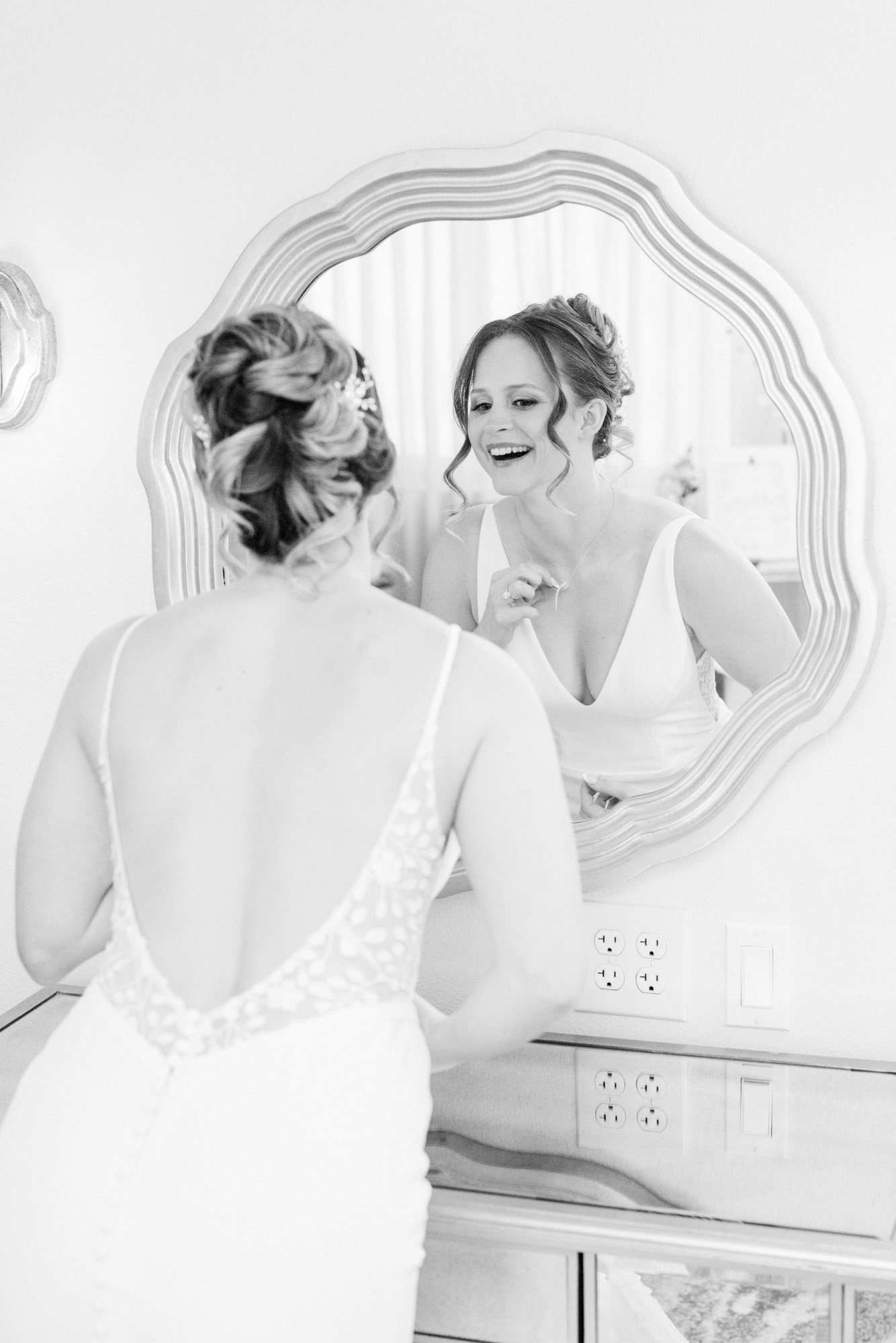 Black-and-white photo of the bride smiling at herself in a mirror before the wedding.