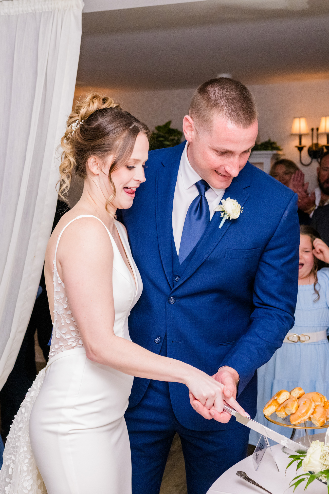 Close-up of the newlyweds cutting their wedding cake as guests watch.