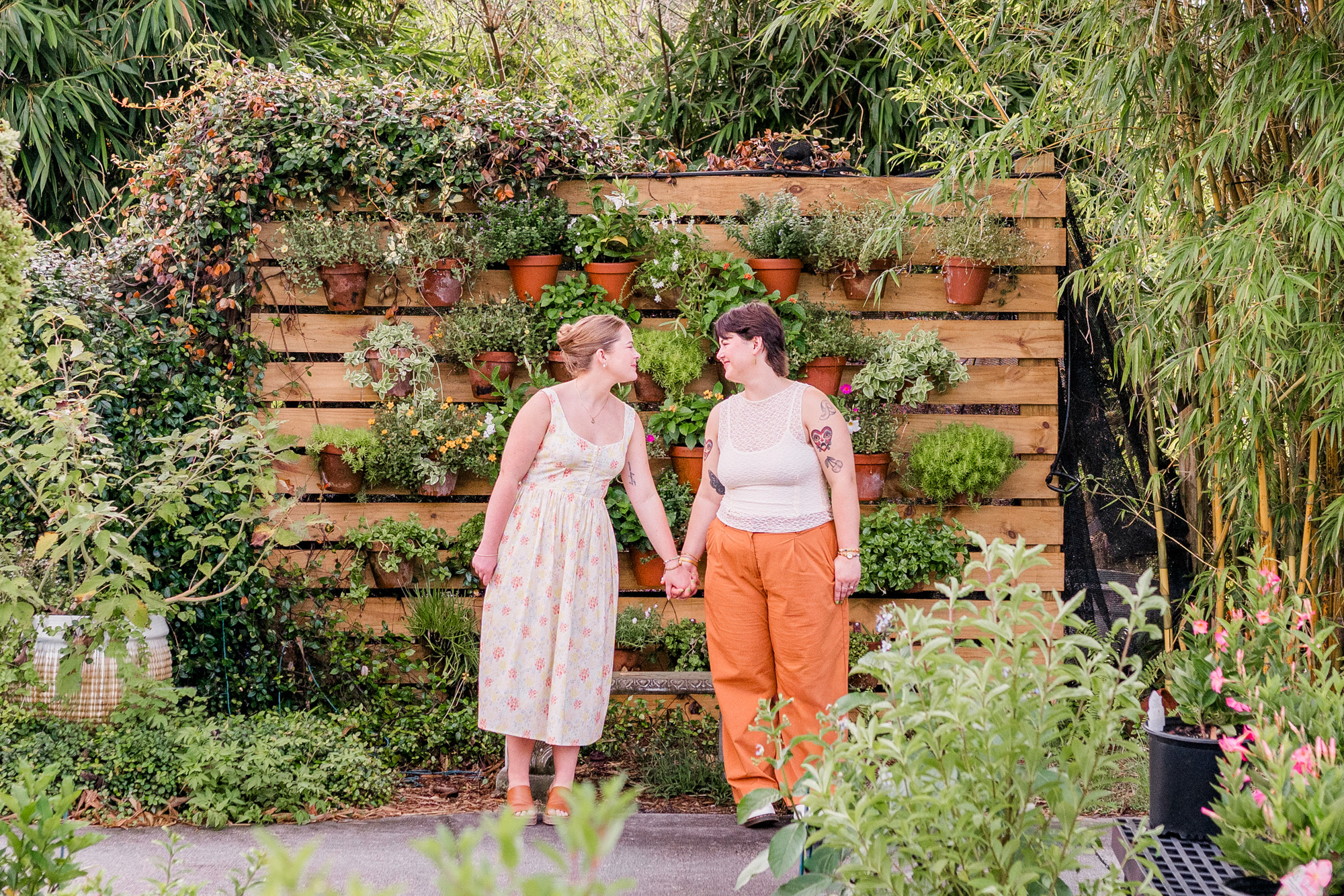 Couple holding hands in front of foliage wall