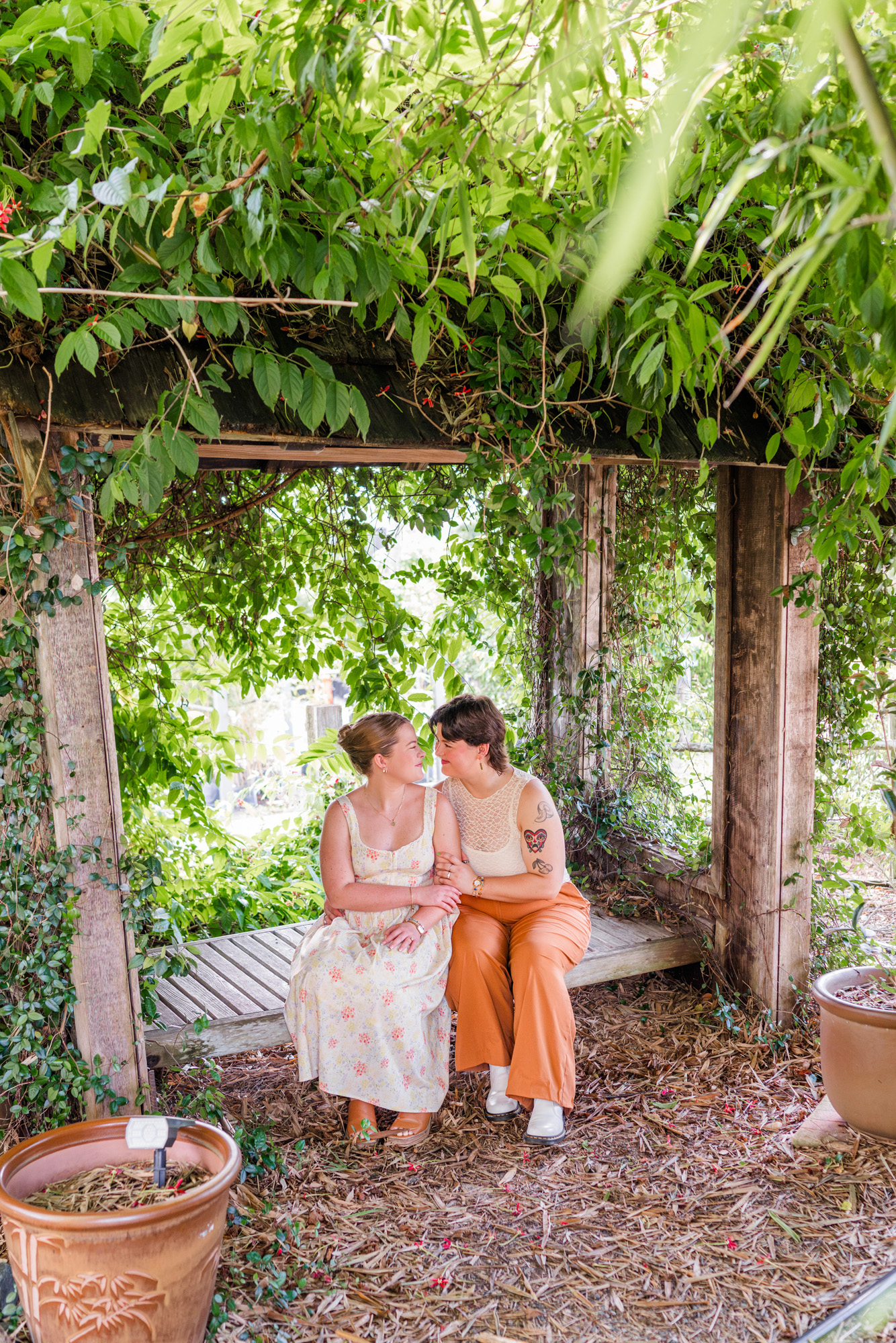 Same sex couple sitting on bench surrounded by greenery