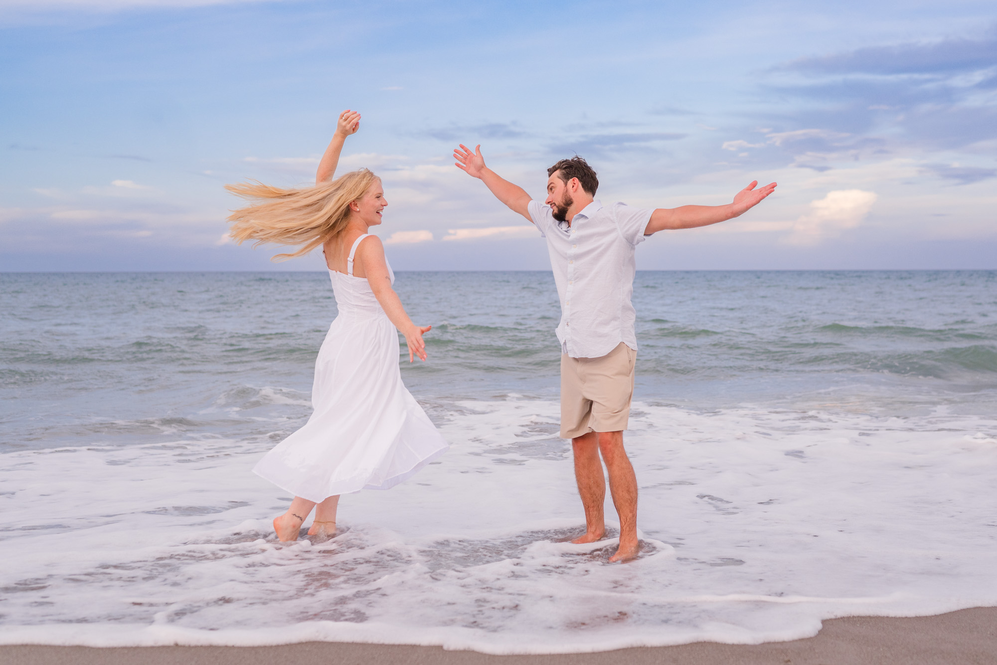 Man and woman having fun with arms in the air by the edge of the ocean
