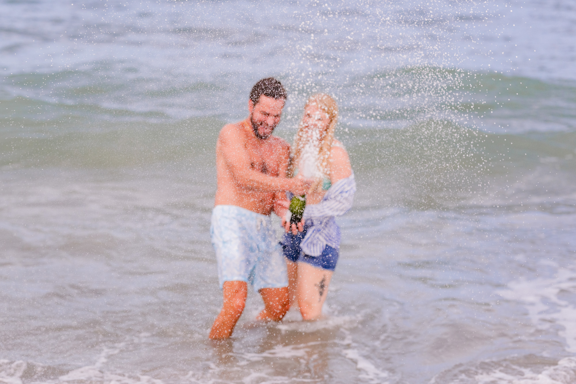 Couple opening champagne in the water during their engagement session