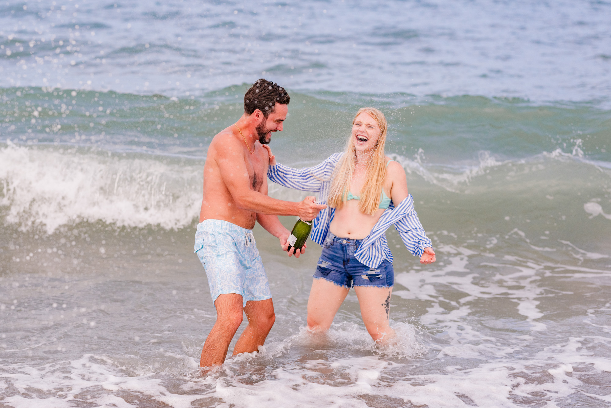 couple laughing while holding a bottle of champagne during their engagement session