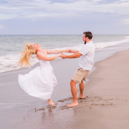 Man and women in a white dress spinning on the beach during an engagement session