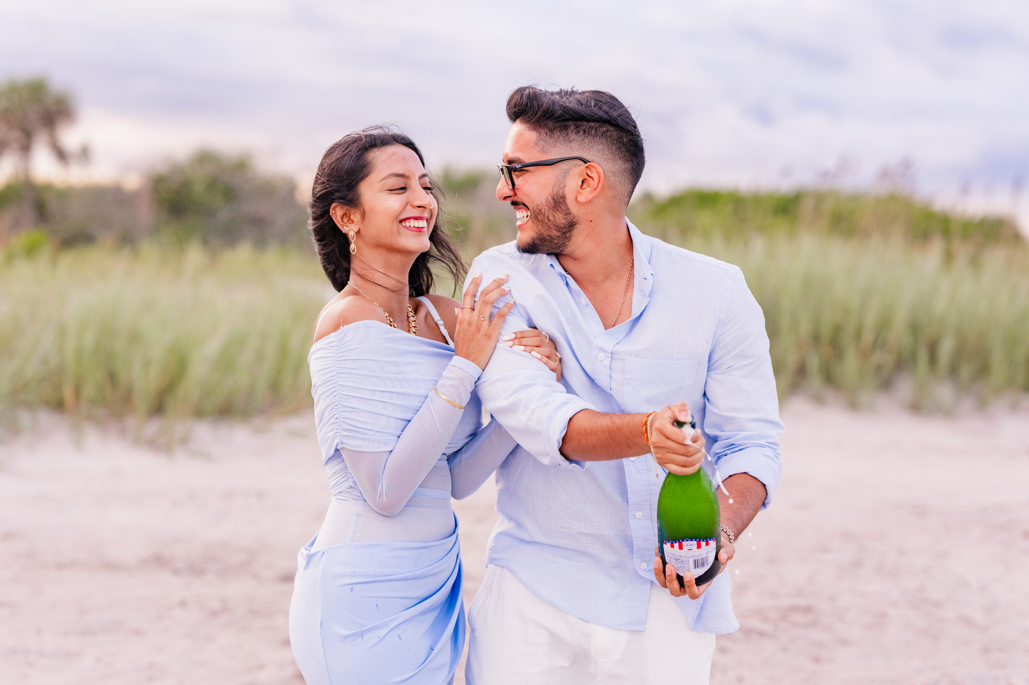 woman hugging onto man who is about to pop a bottle of champagne on Cocoa Beach