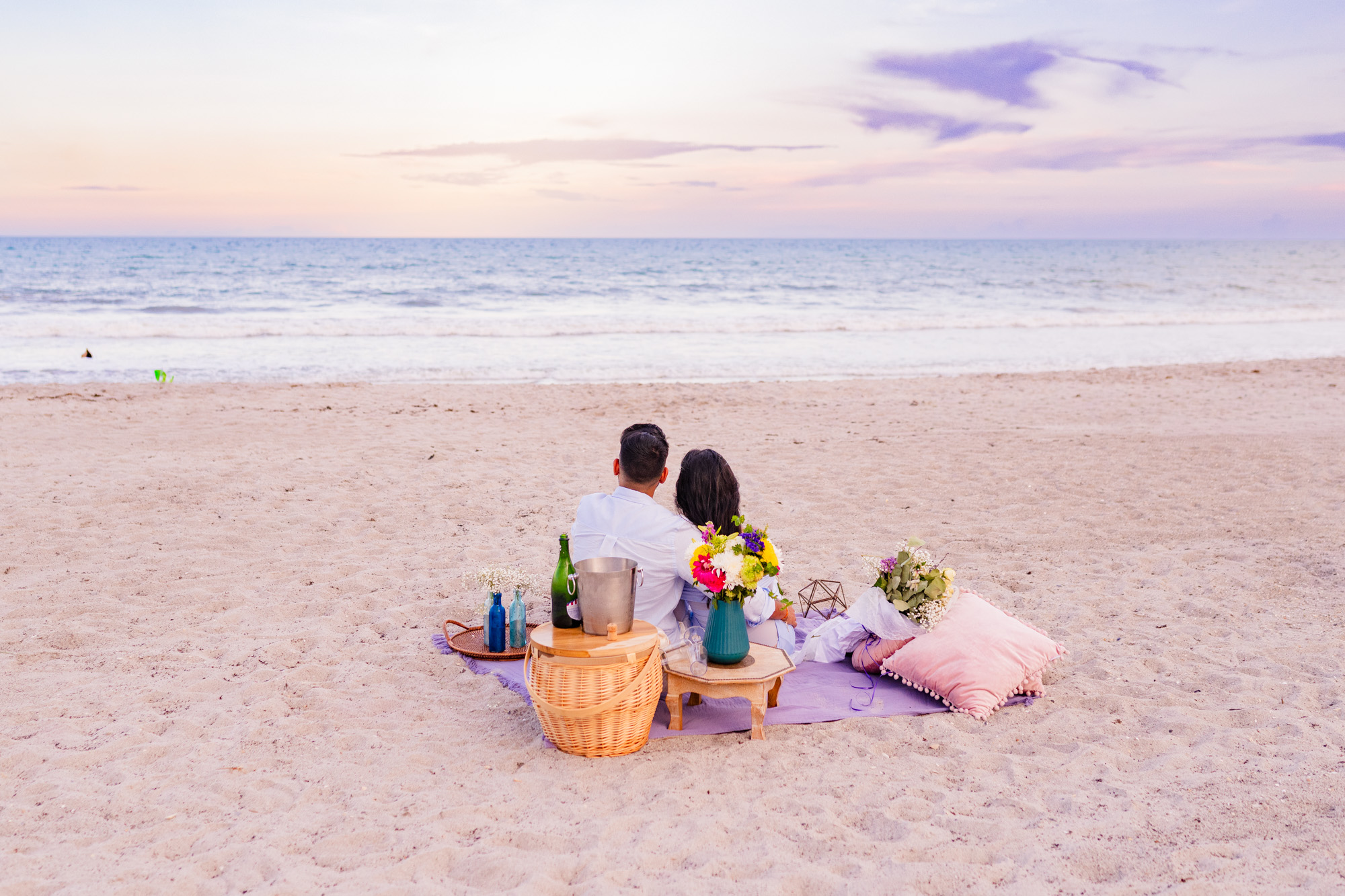 Man and woman looking off to the ocean while sitting on a blanket after he asked her to marry him